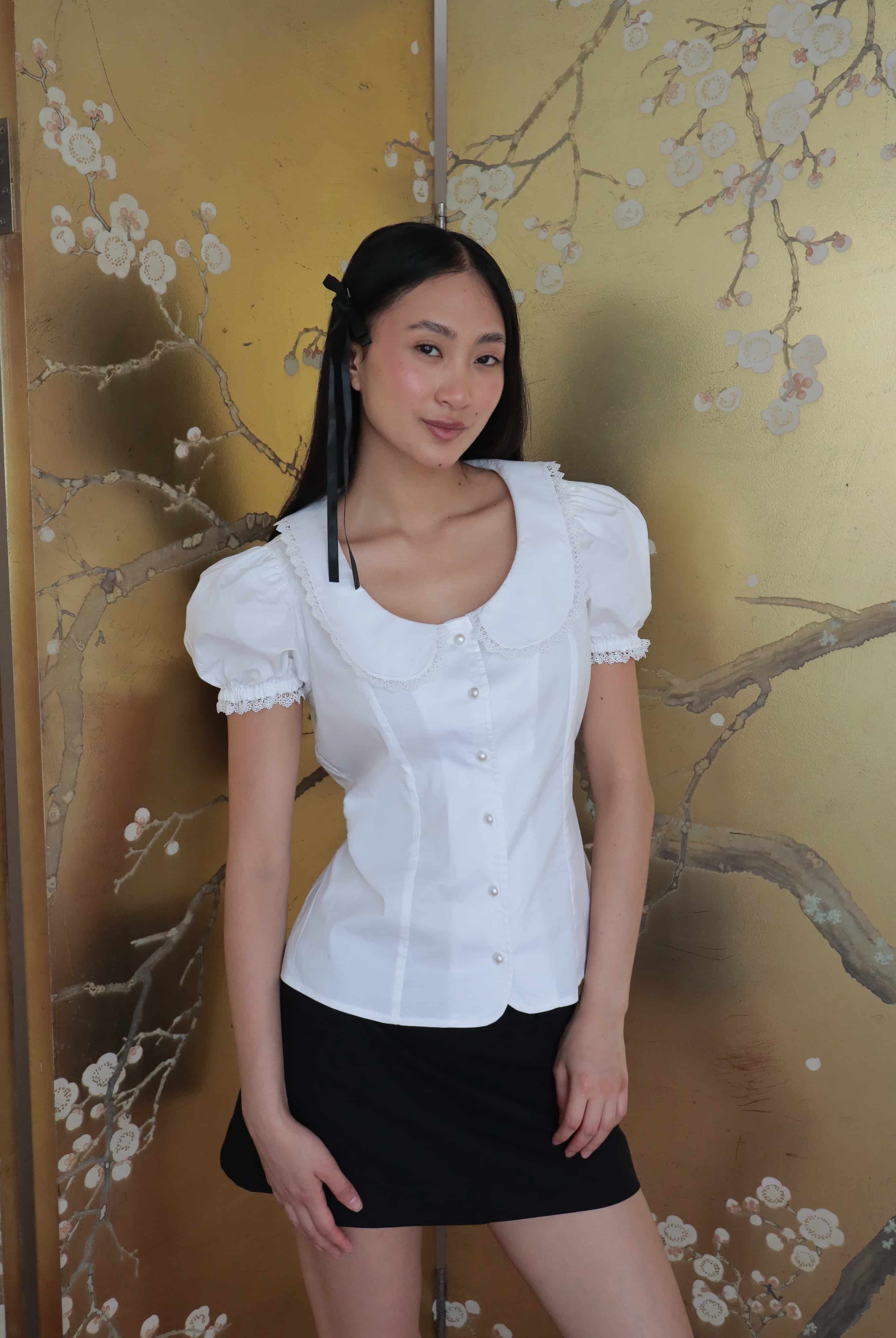 Mujer con blusa blanca escotada y falda negra. Posando en fondo dorado con diseño floral