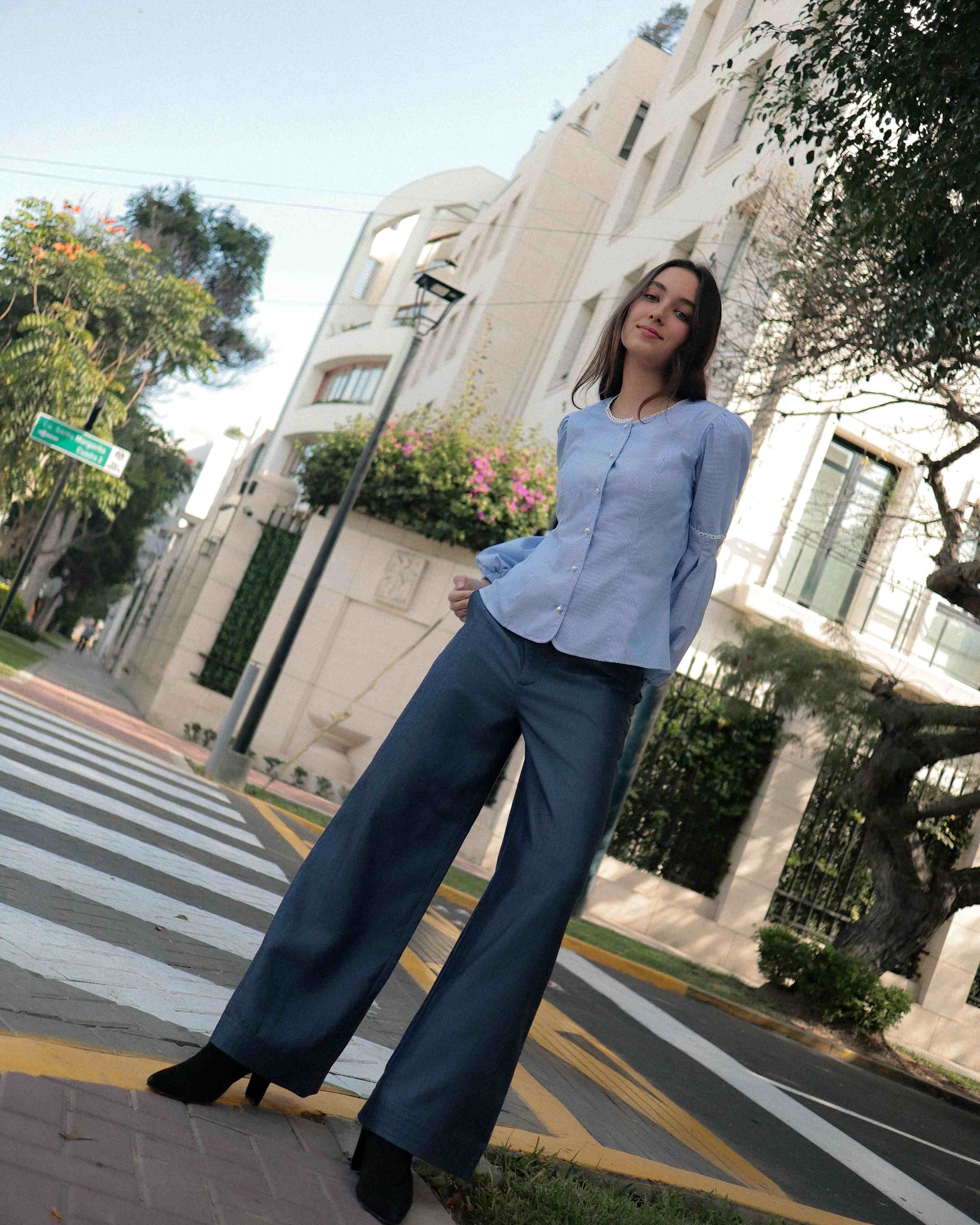 Mujer con blusa a rayas celeste con detalles tejidos, cuello redondo y mangas ligeramente voluminosas. Posando en la calle.