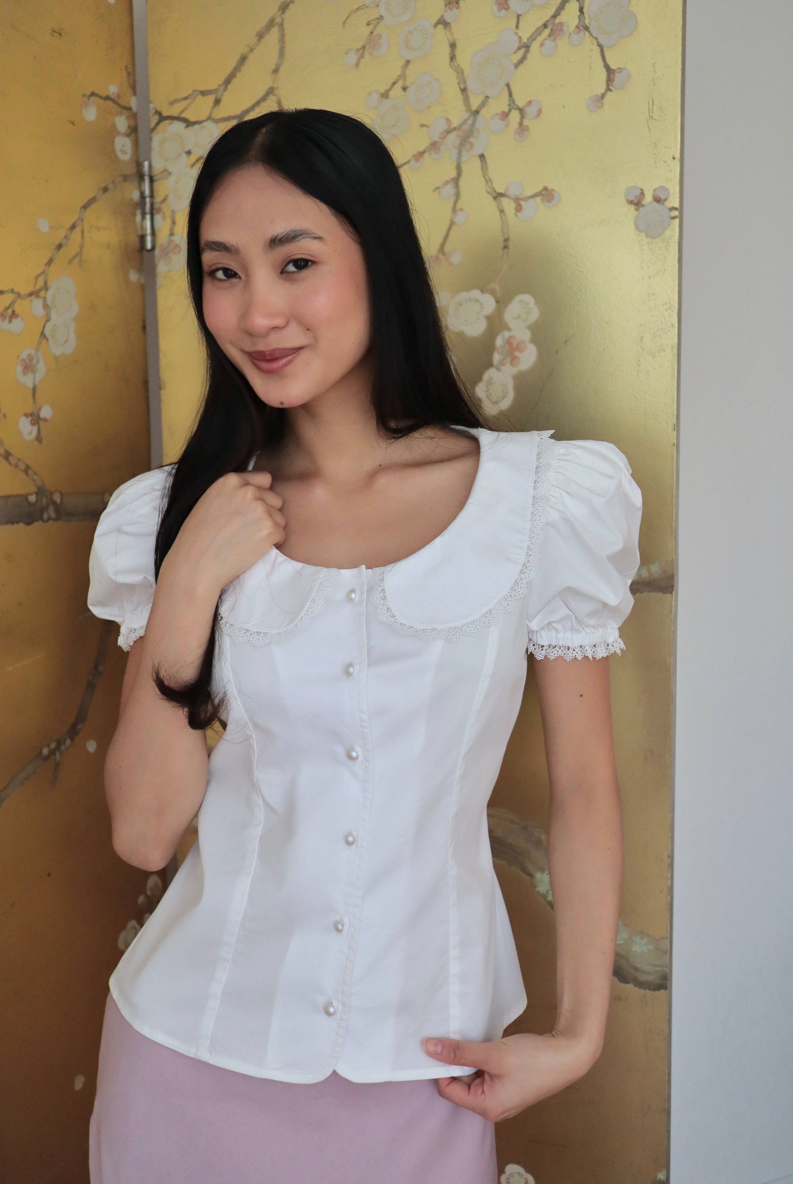 Mujer con blusa blanca escotada y falda rosa midi. Posando en fondo dorado con diseño floral