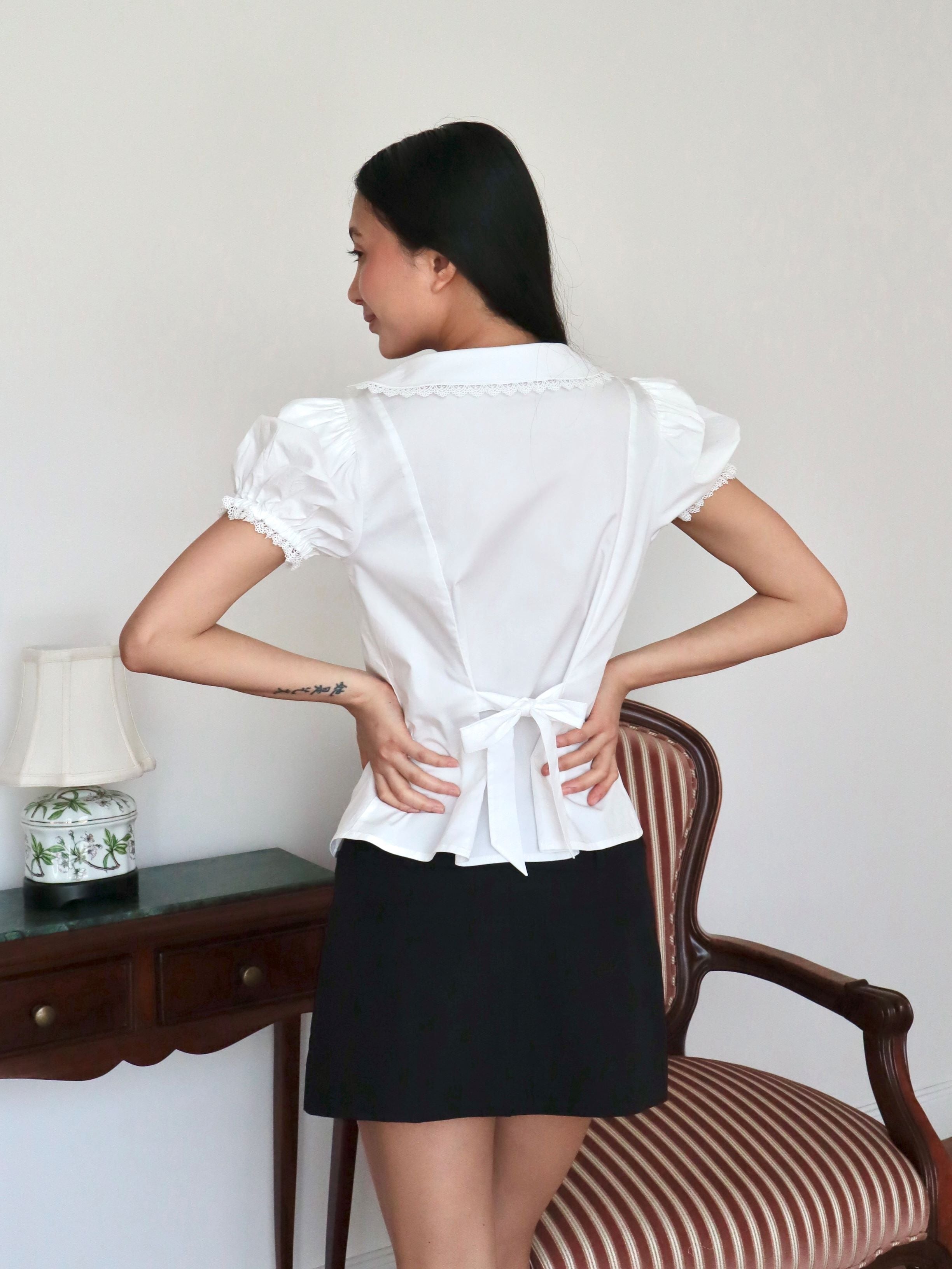 Mujer de espaldas con blusa blanca escotada y lazo.