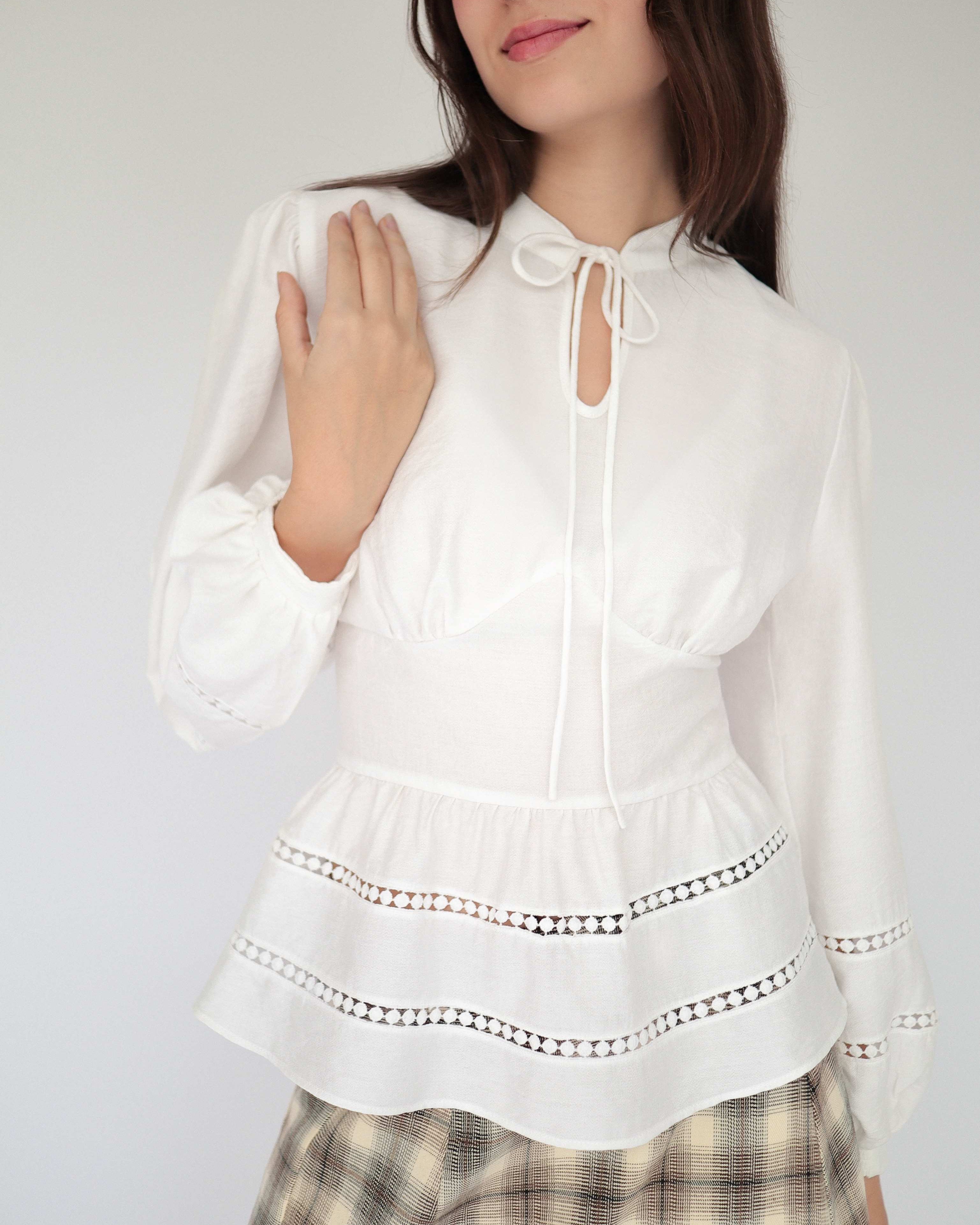 Blusa blanca sofisticada y elegante estilo peplum ceñida, con cuello alto y detalles tejidos.