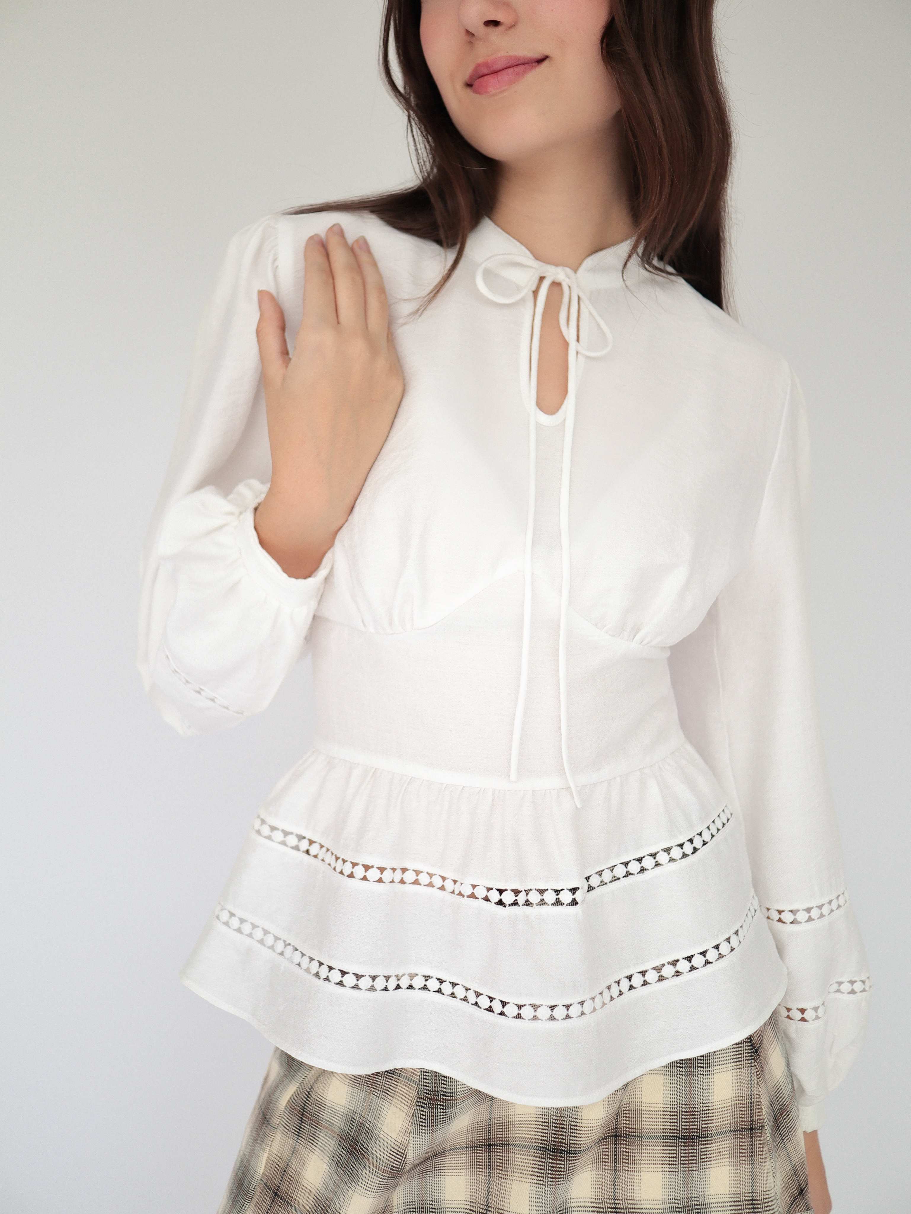 Blusa blanca sofisticada y elegante estilo peplum ceñida, con cuello alto y detalles tejidos.