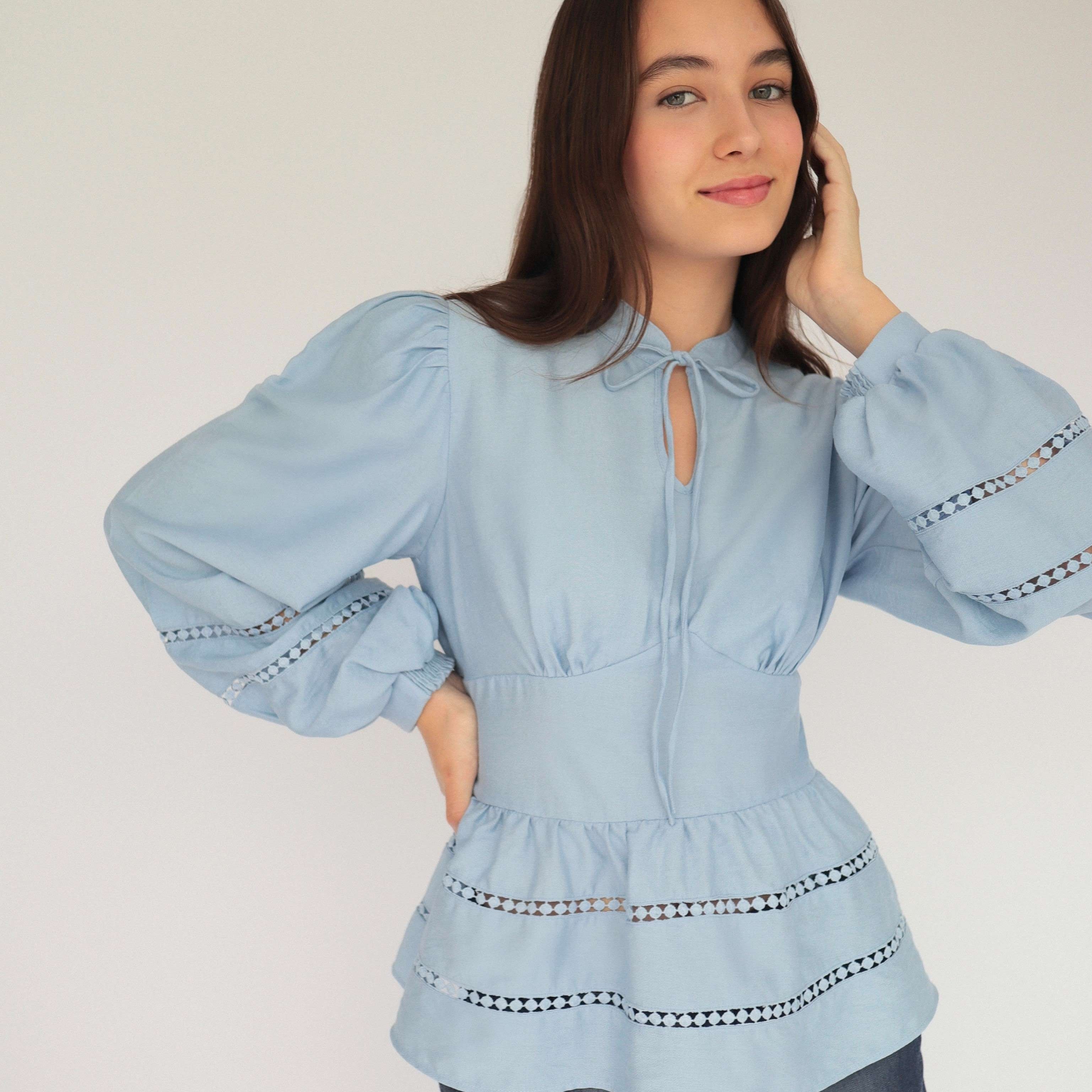 Mujer con blusa celeste y pantalones estilo denim posando en fondo blanco.