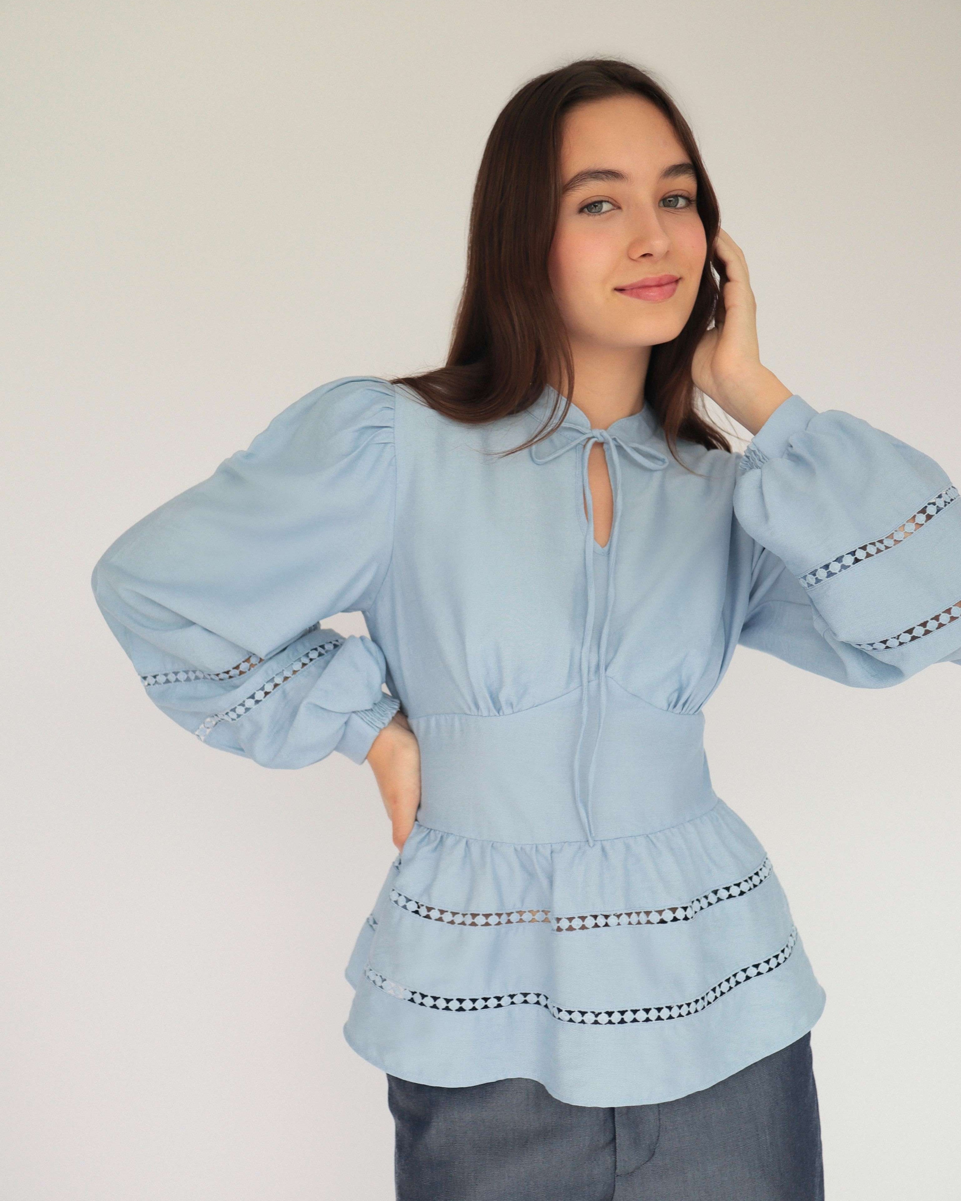 Mujer con blusa celeste y pantalones estilo denim posando en fondo blanco.