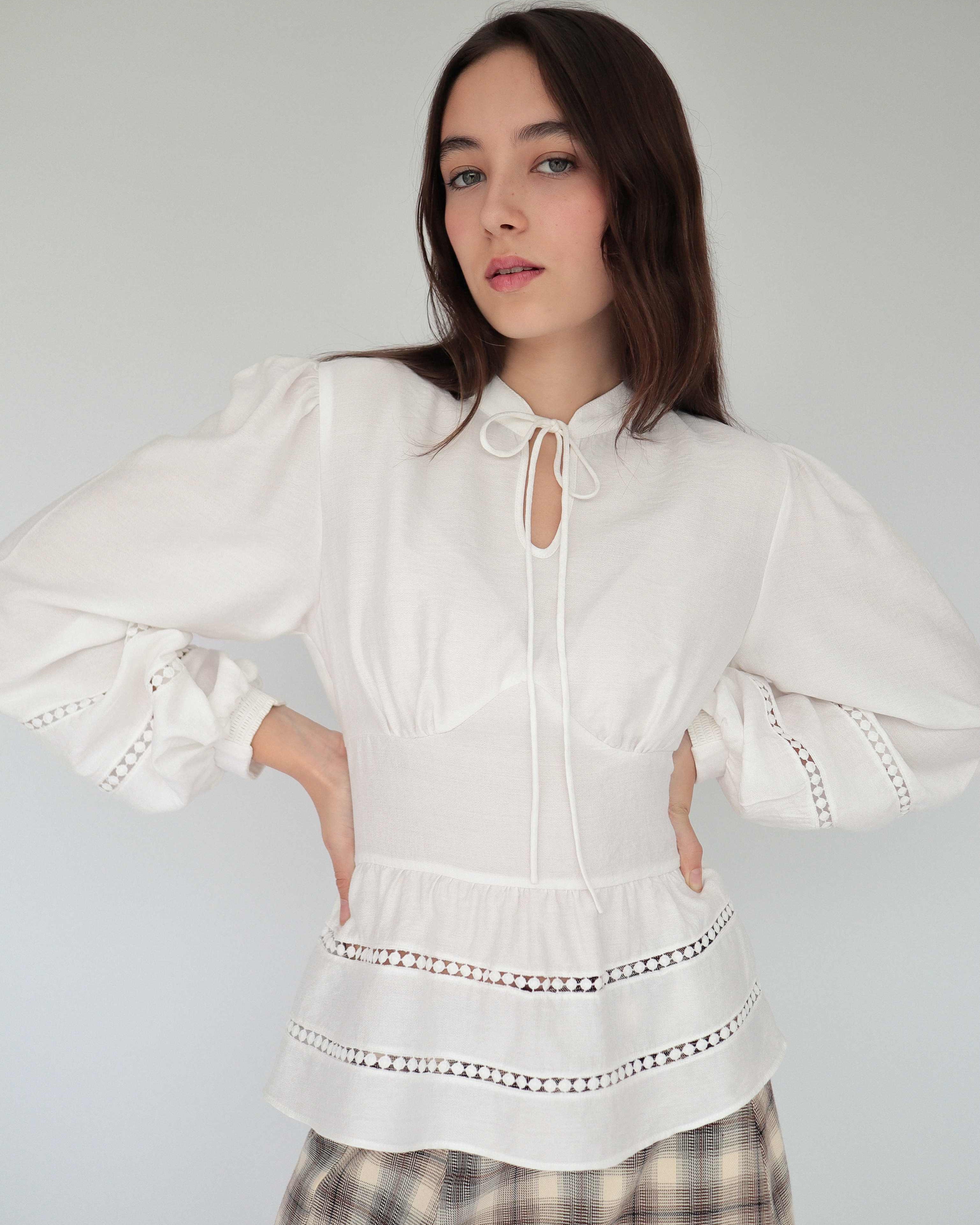 Modelo con blusa blanca estilo peplum ceñida, con cuello alto y detalles tejidos.