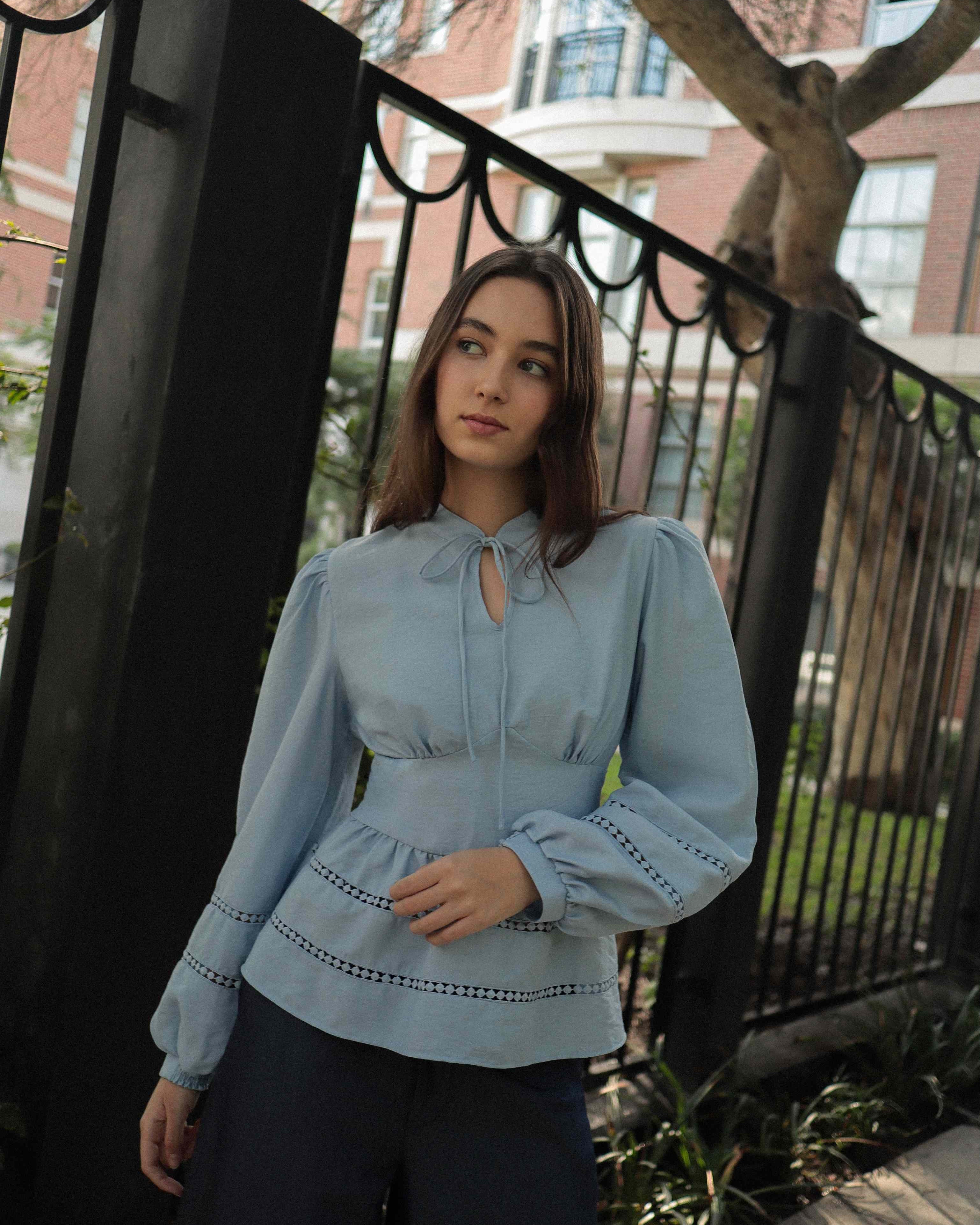 Mujer con blusa celeste con detalles tejidos y pantalones estilo denim posando en calle