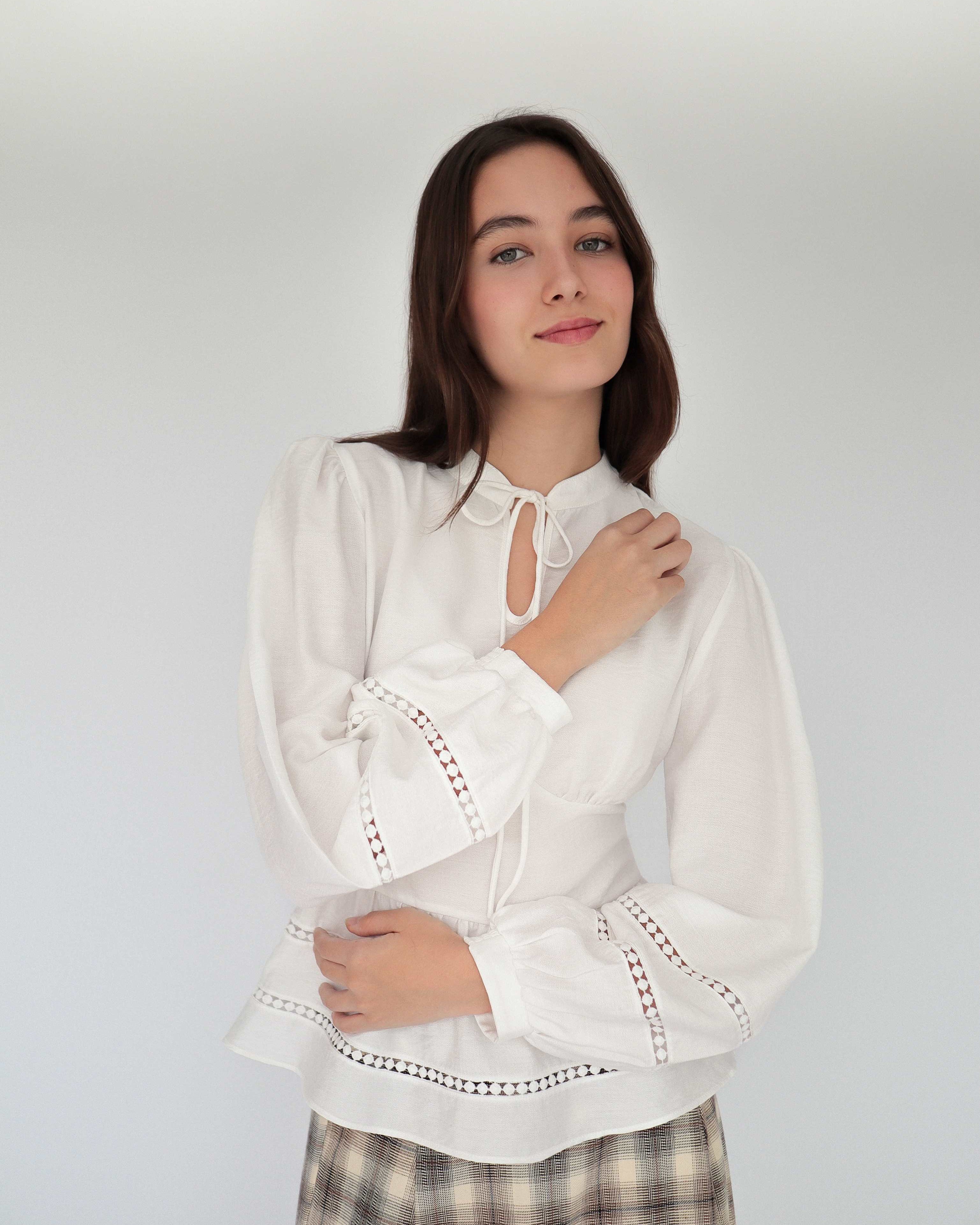 Modelo con blusa blanca sofisticada estilo peplum ceñida, con cuello alto y detalles tejidos.