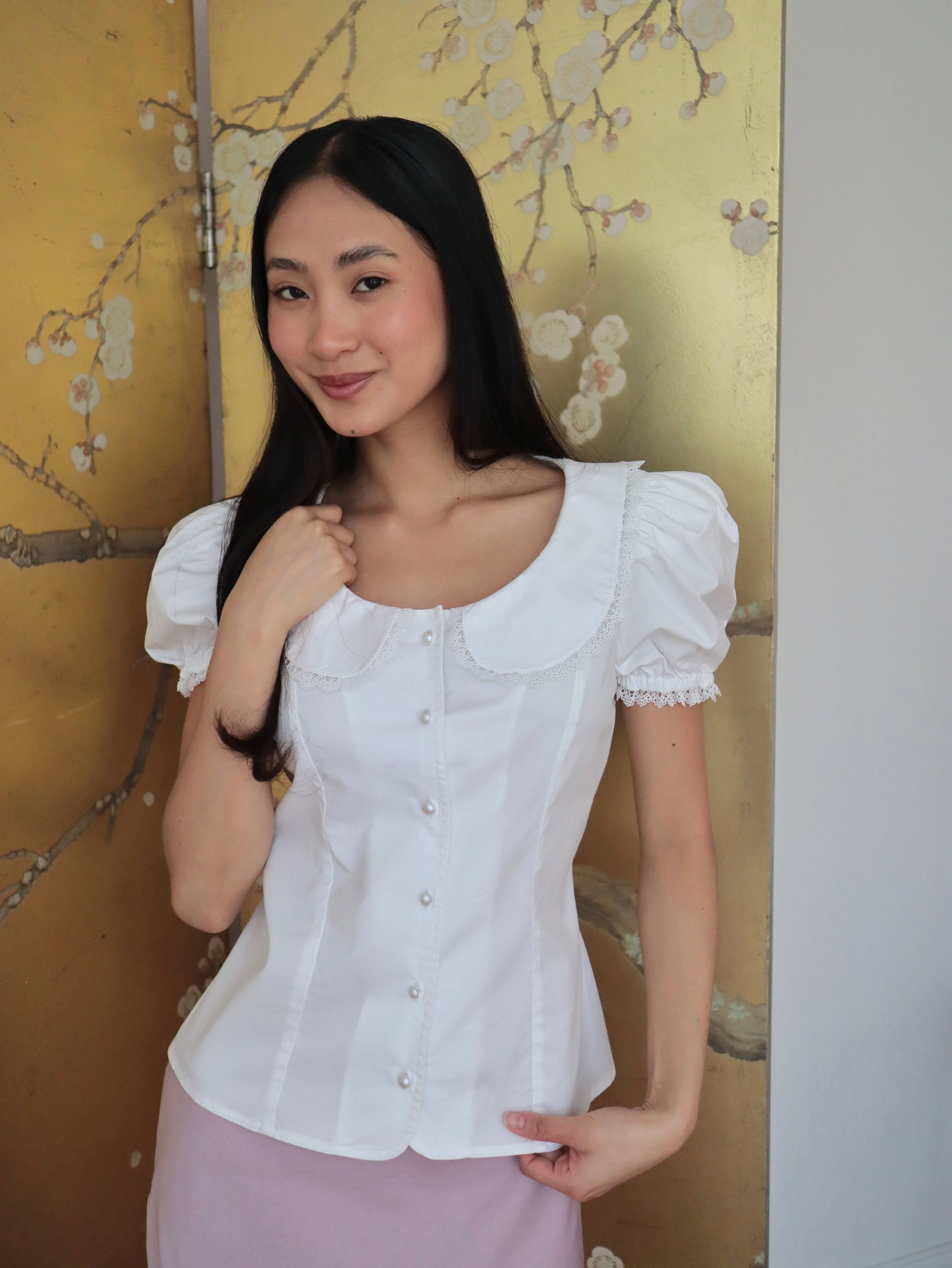 Mujer con blusa blanca escotada y falda rosa midi. Posando en fondo dorado con diseño floral