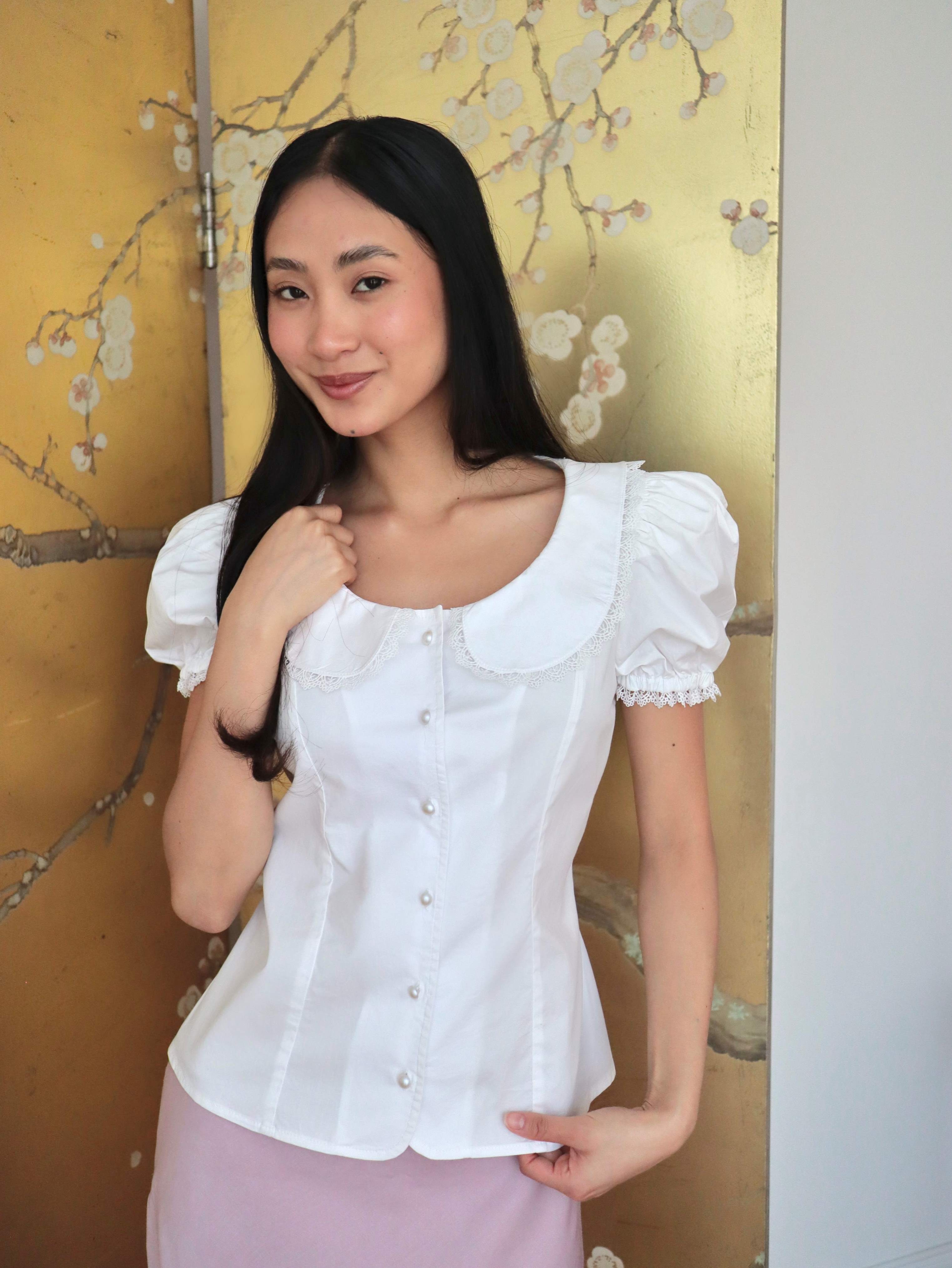 Mujer con blusa blanca escotada y falda rosa midi. Posando en fondo dorado con diseño floral