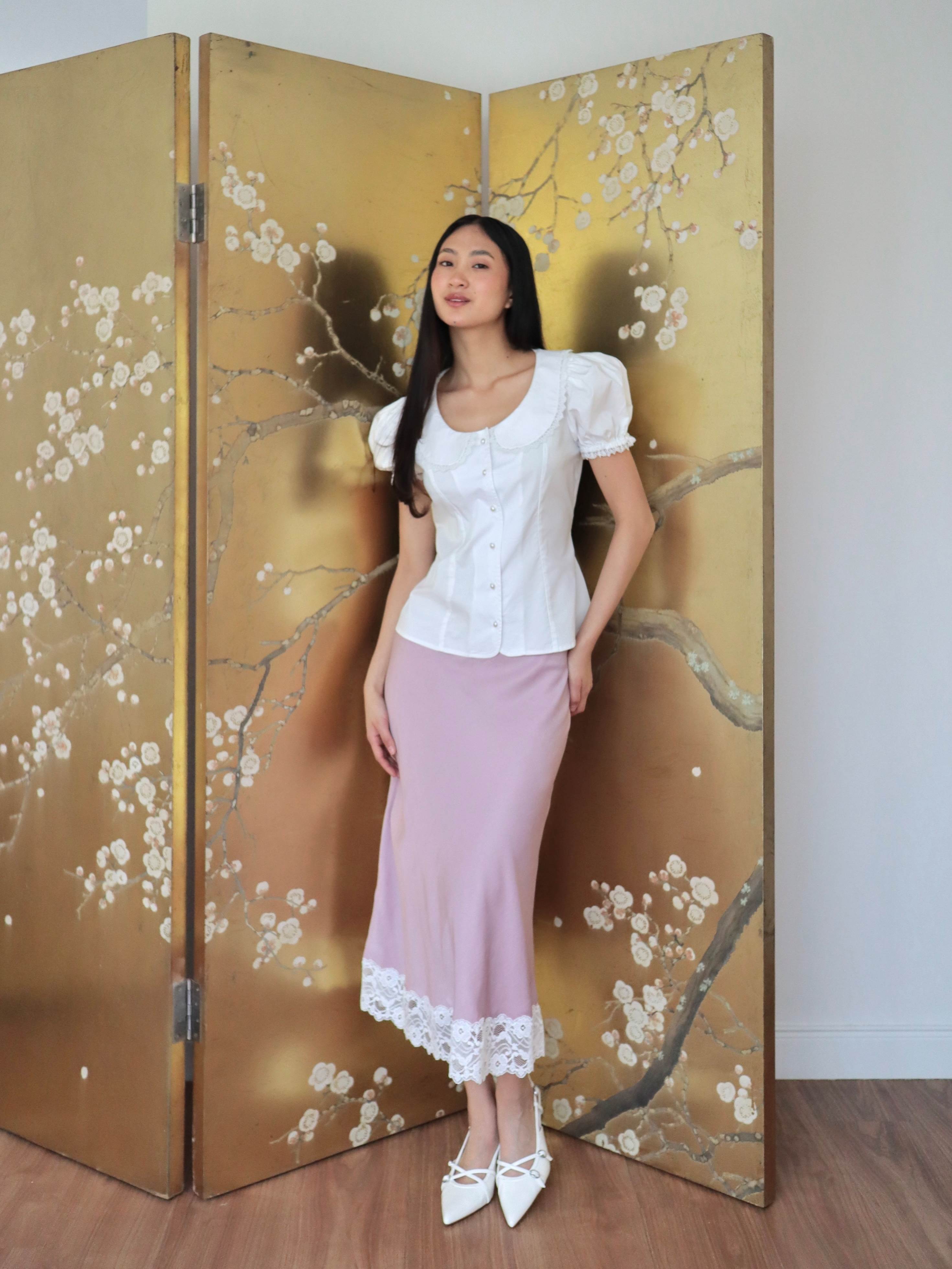 Mujer con blusa blanca escotada y falda rosa midi estilo lencero.