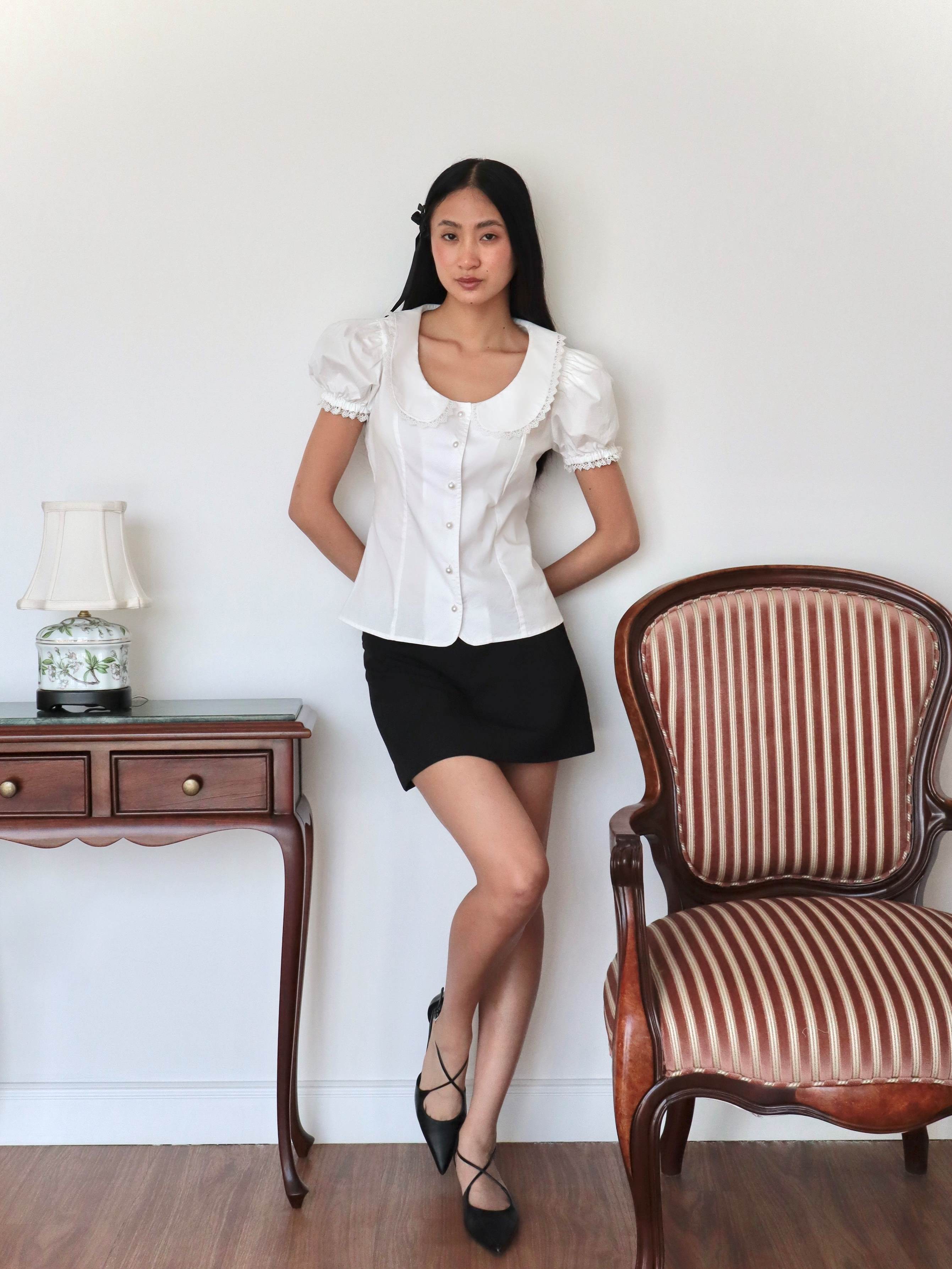 Mujer con blusa blanca escotada y falda rosa midi. Posando en fondo vintage.