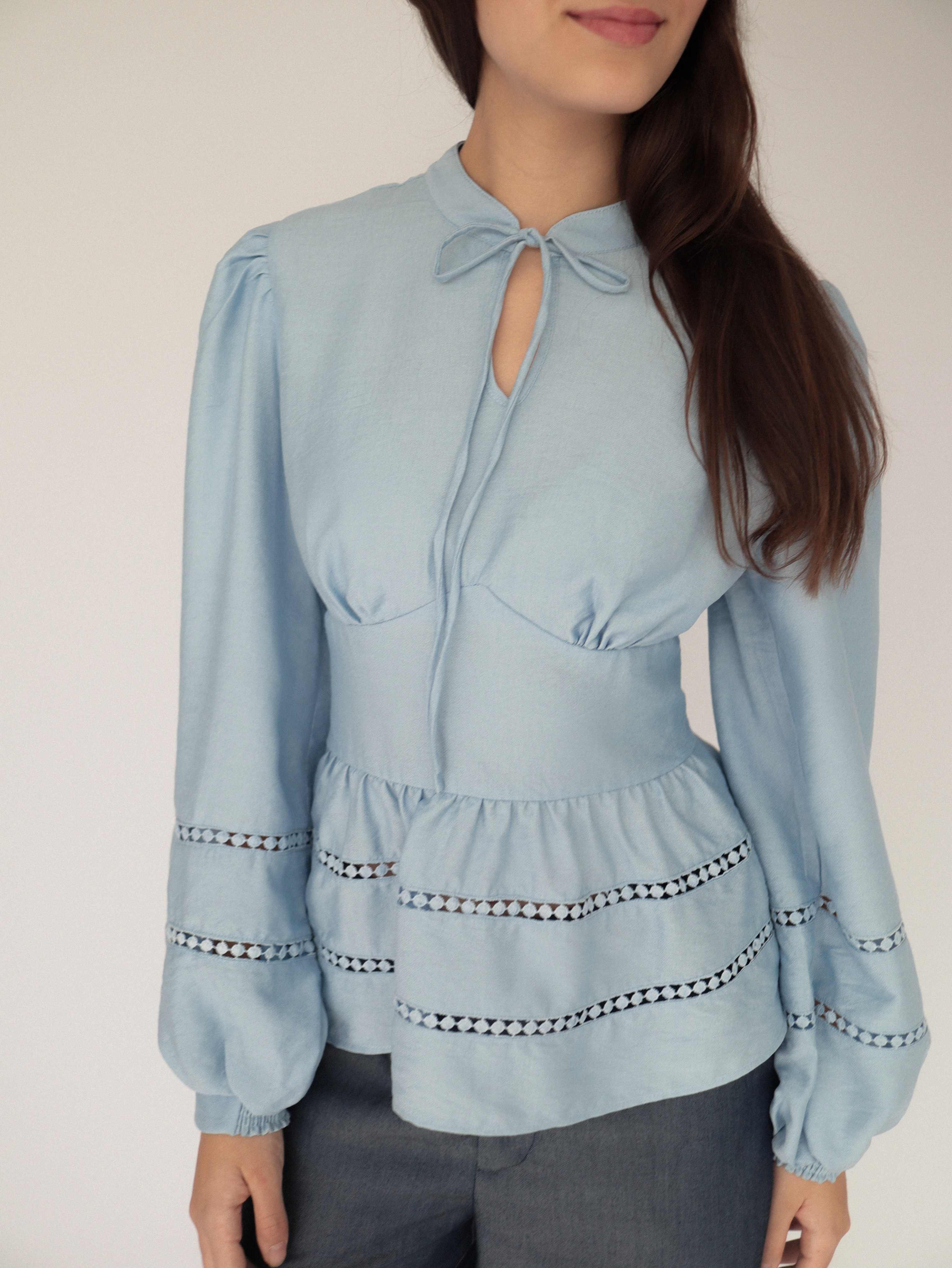 Blusa celeste estilo peplum, cuello alto y detalles tejidos.