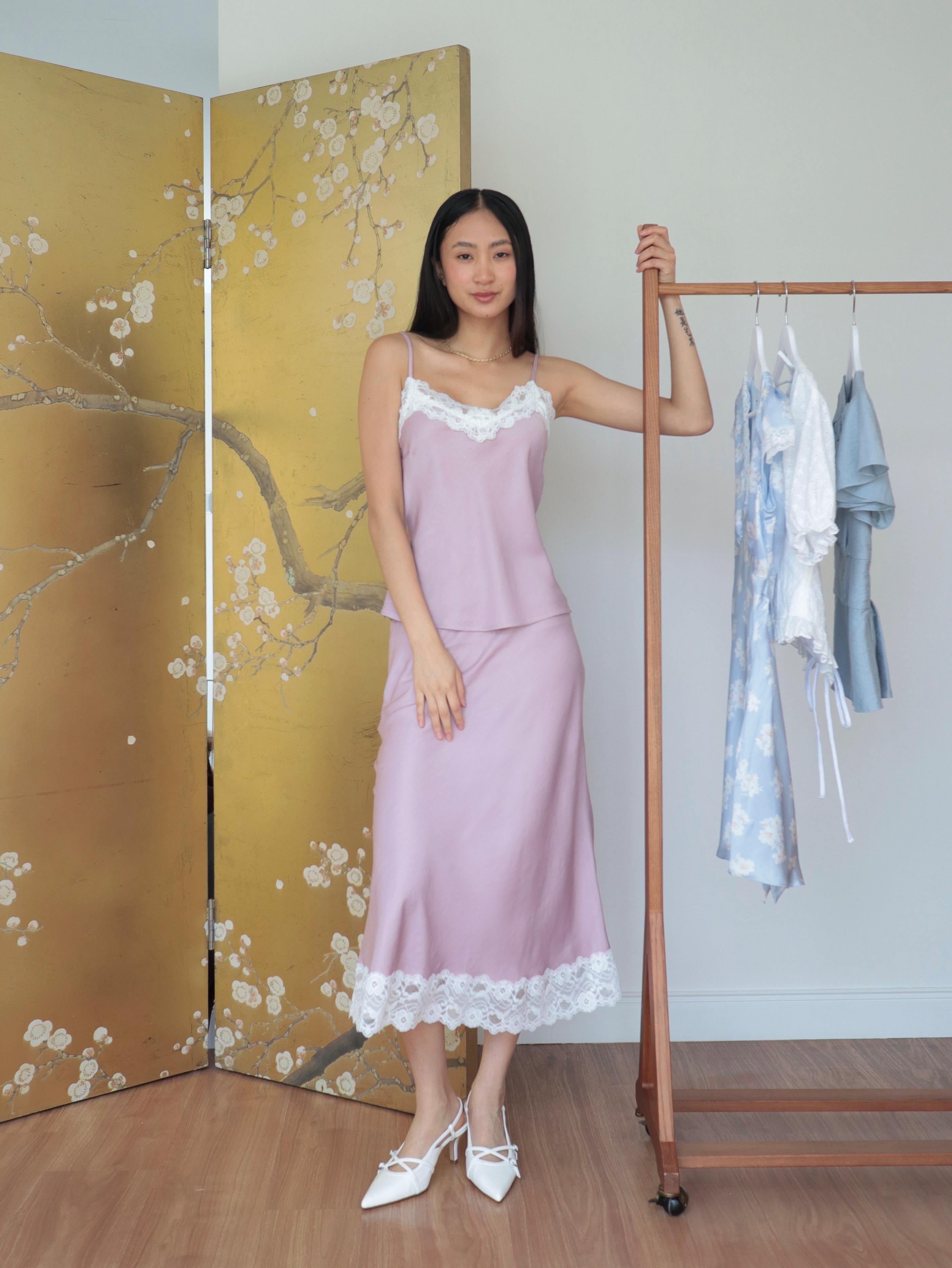 Mujer usando conjunto de top y falda midi lencero rosa romántico en fondo floral y rack de ropa
