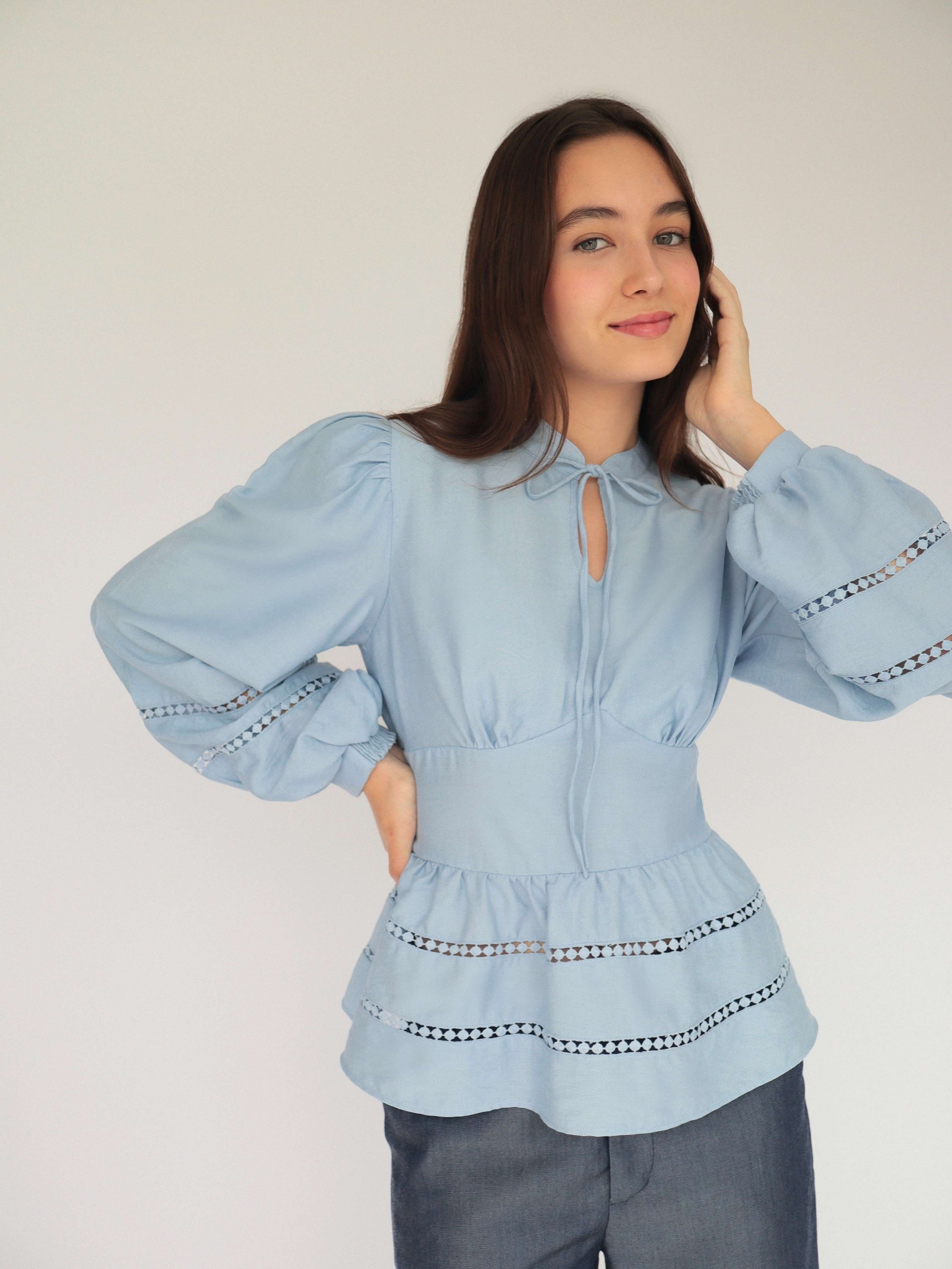 Mujer con blusa celeste y pantalones estilo denim posando en fondo blanco.