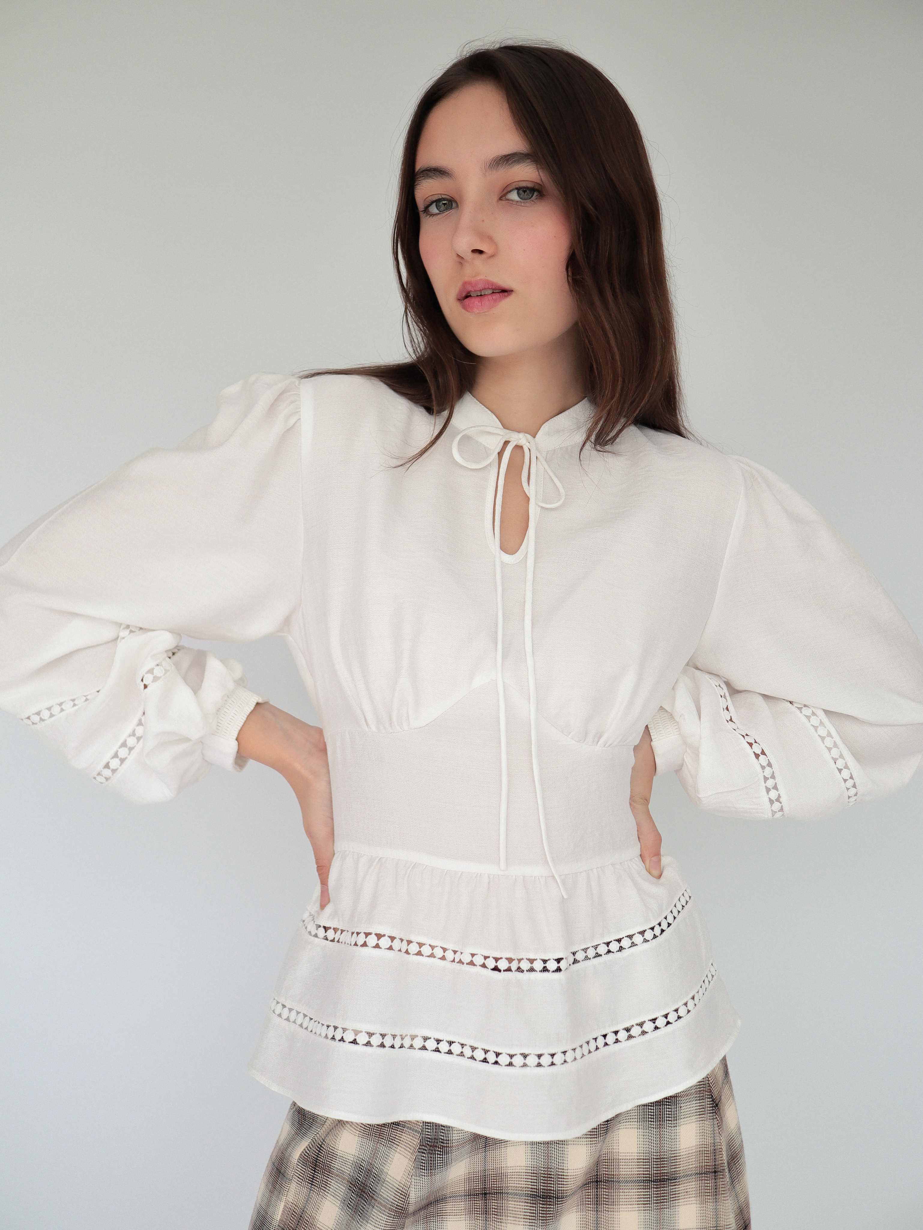 Modelo con blusa blanca estilo peplum ceñida, con cuello alto y detalles tejidos.