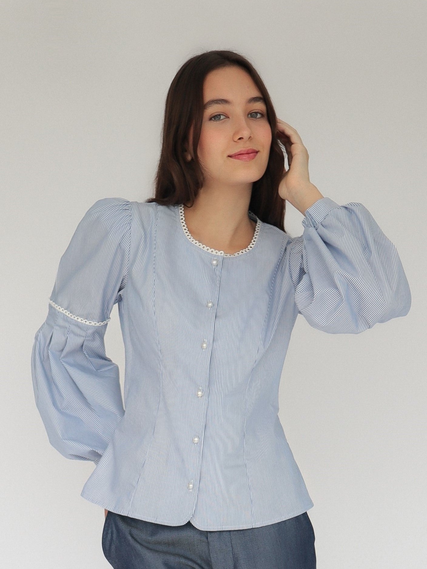 Mujer con blusa a rayas celeste con detalles tejidos, cuello redondo y mangas ligeramente voluminosas.  Posando en fondo blanco.