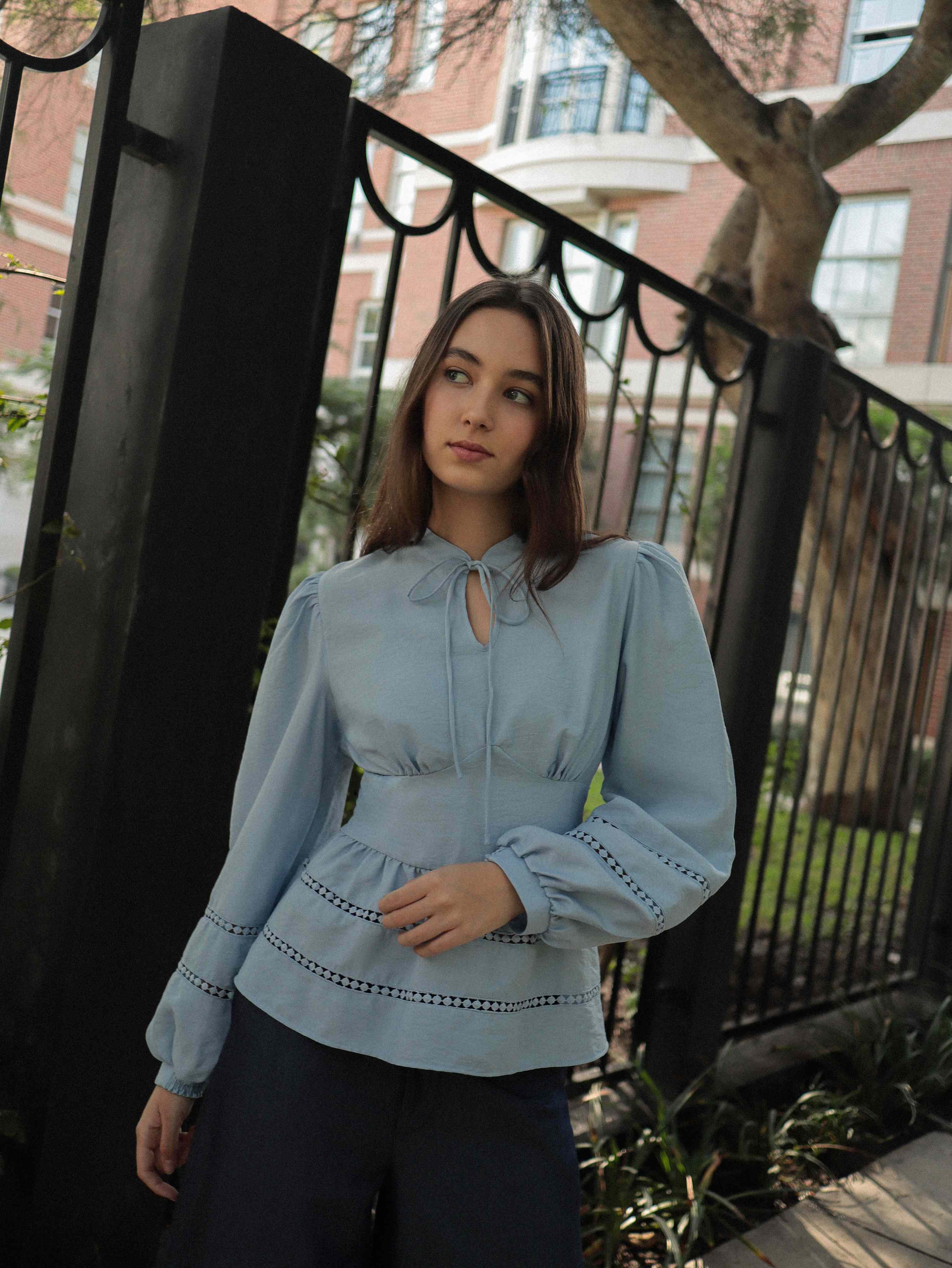 Mujer con blusa celeste con detalles tejidos y pantalones estilo denim posando en calle