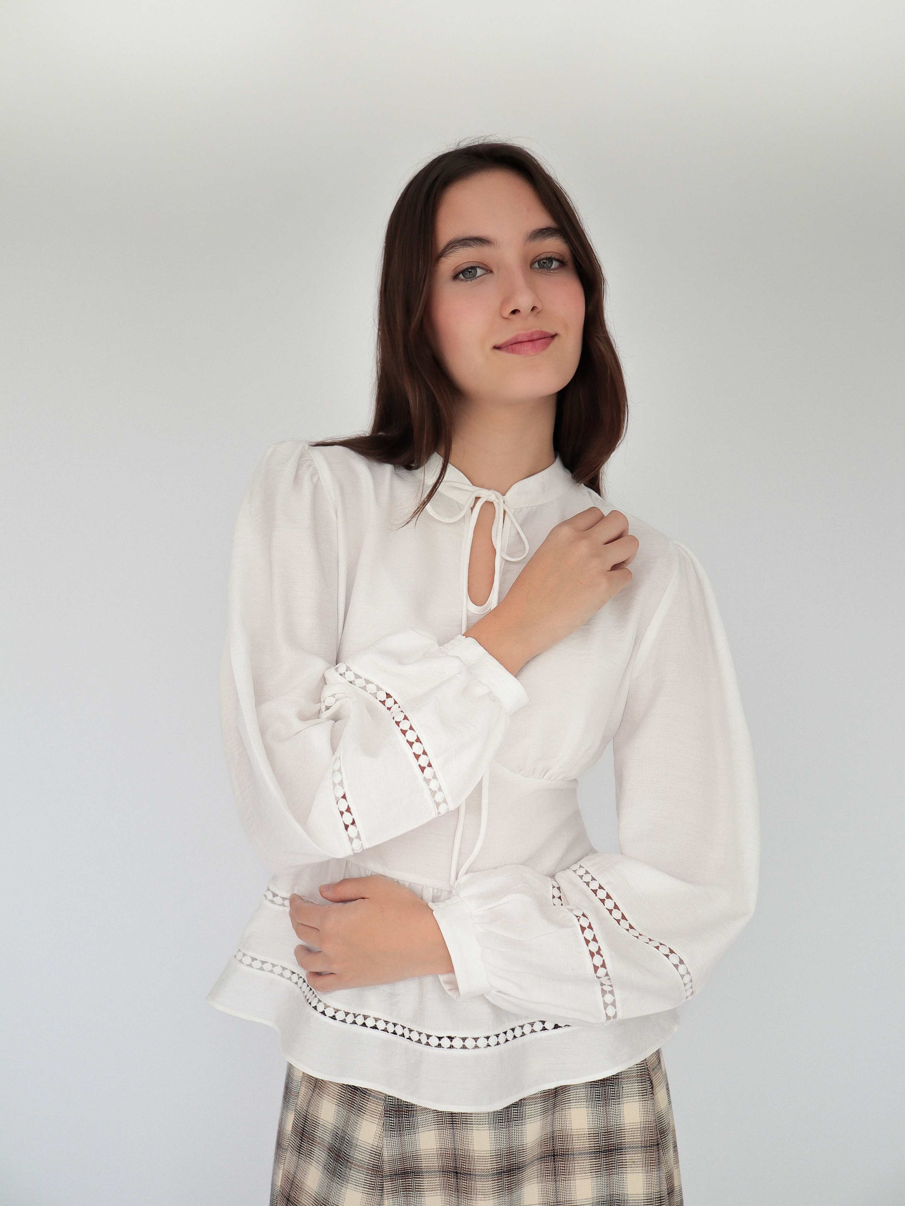 Modelo con blusa blanca sofisticada estilo peplum ceñida, con cuello alto y detalles tejidos.