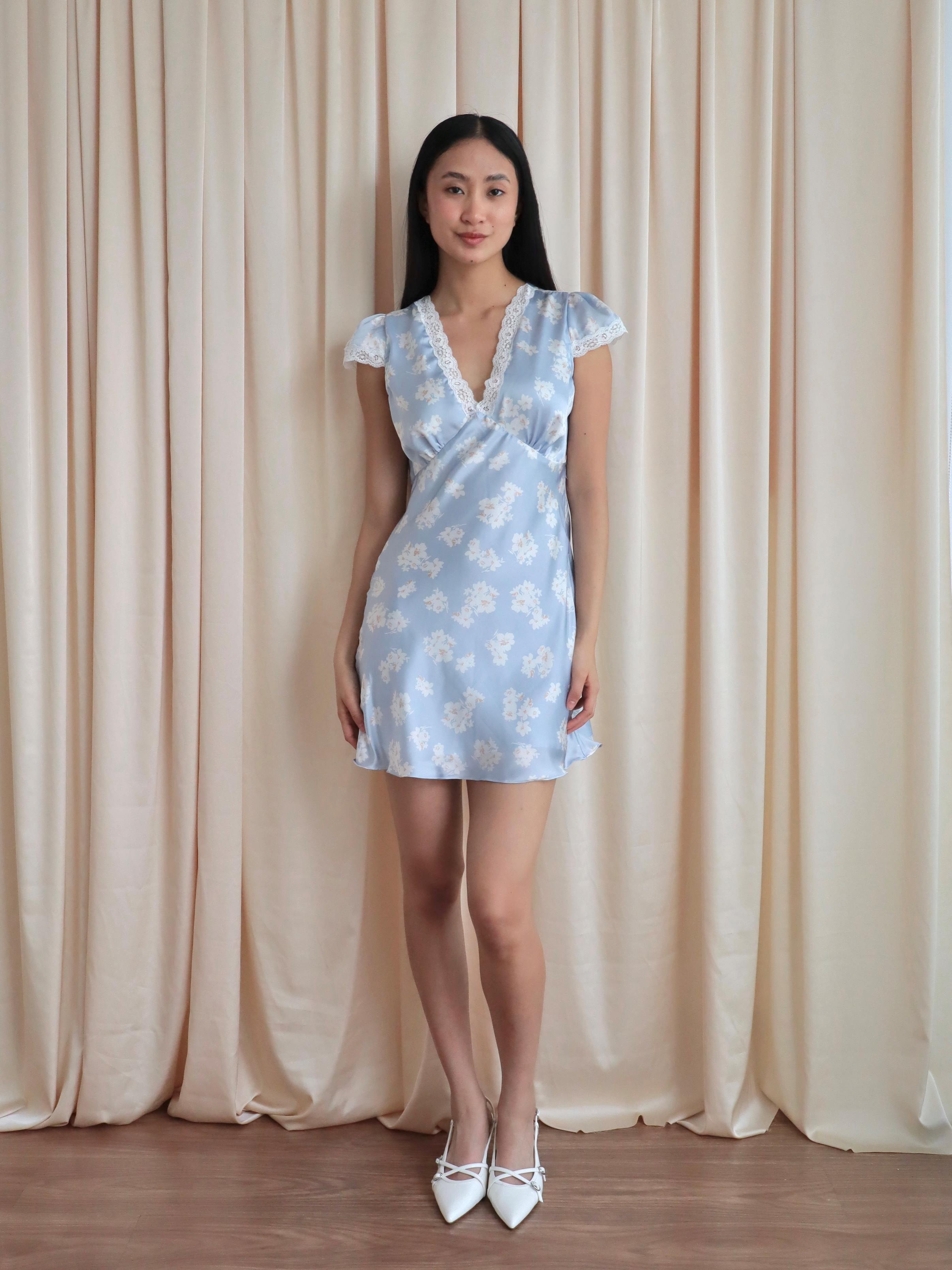 mujer en fondo amarillo usando vestido escote V, mangas cortas con blondas hecho de satin celeste estampado con flores blancas 